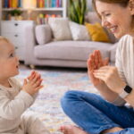 Eine Mutter sitzt mit ihrem Kind am Boden und gebärdet "mehr" mit den Händen